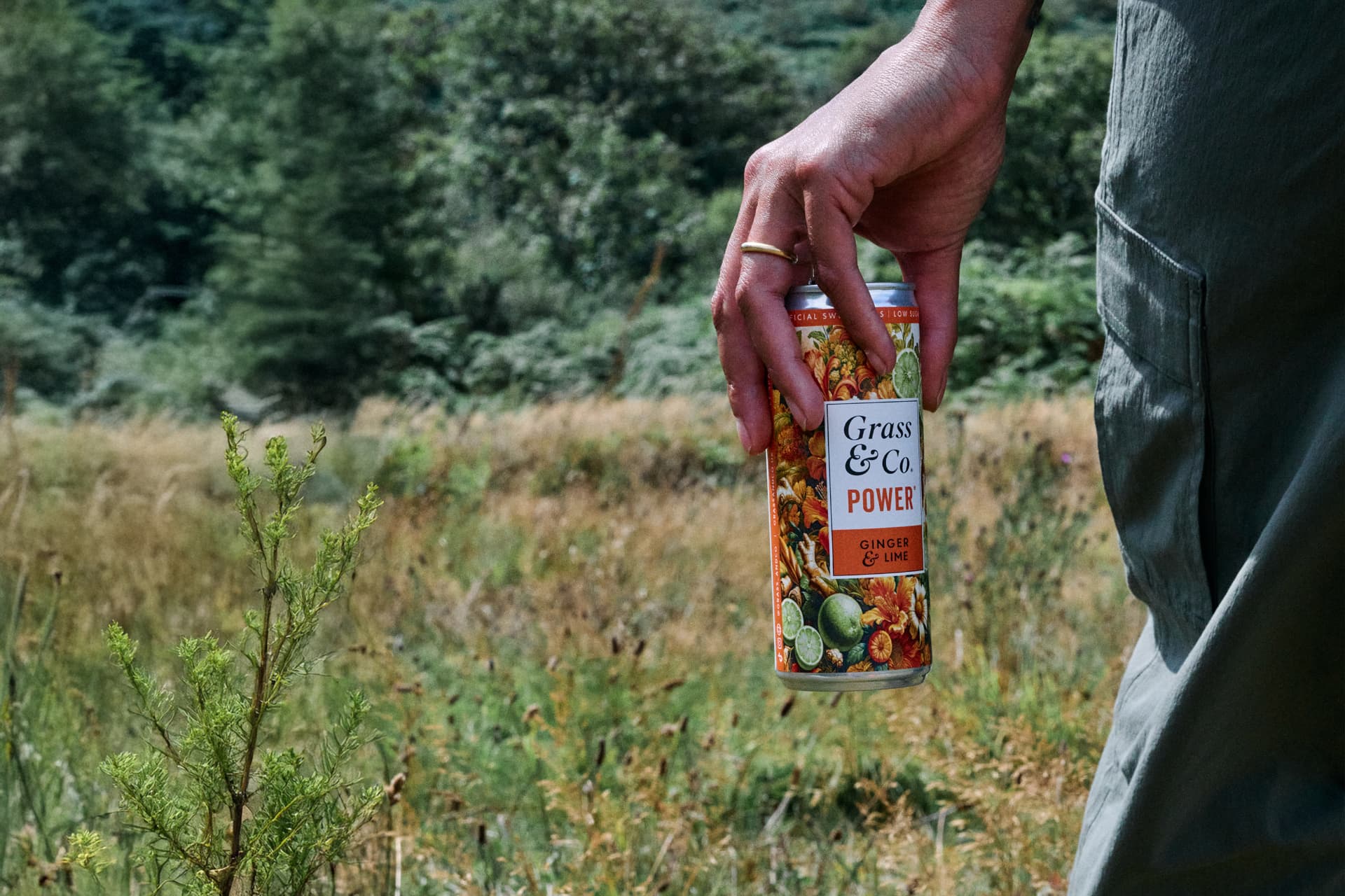 A POWER can dangling from a hand on a grassy trail
