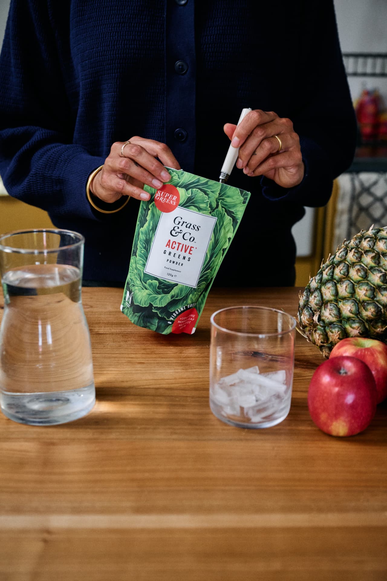 Stirring ACTIVE Greens powder on a wooden counter with pineapple and apples