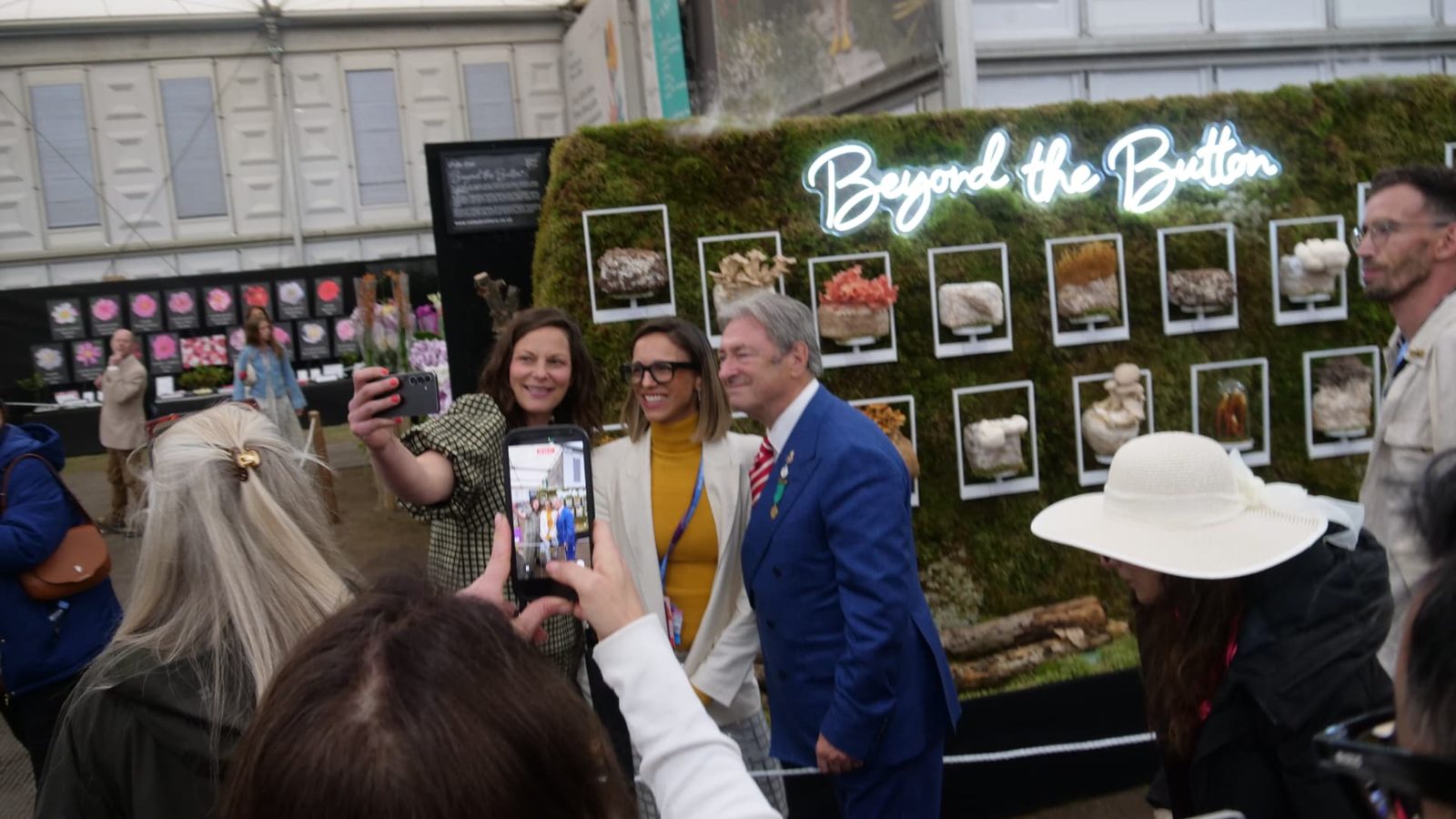 Visitors including Alan Titchmarsh posing for photographs in front of the Beyond the Button exhibit