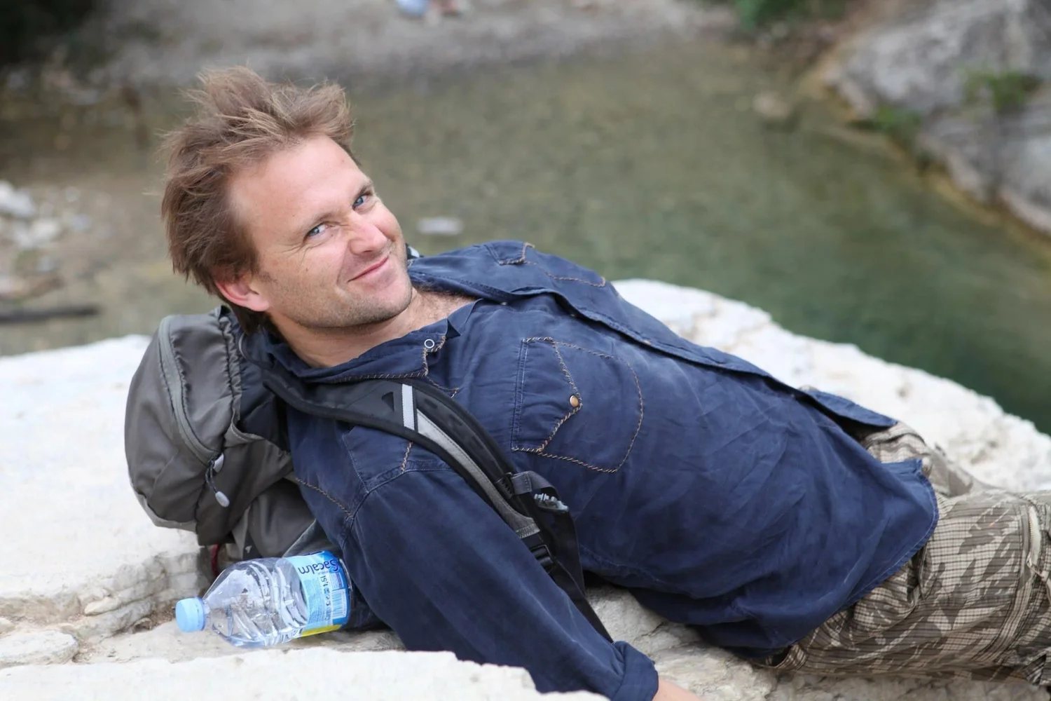 Tom Grass resting on a rock beside a river on an expedition